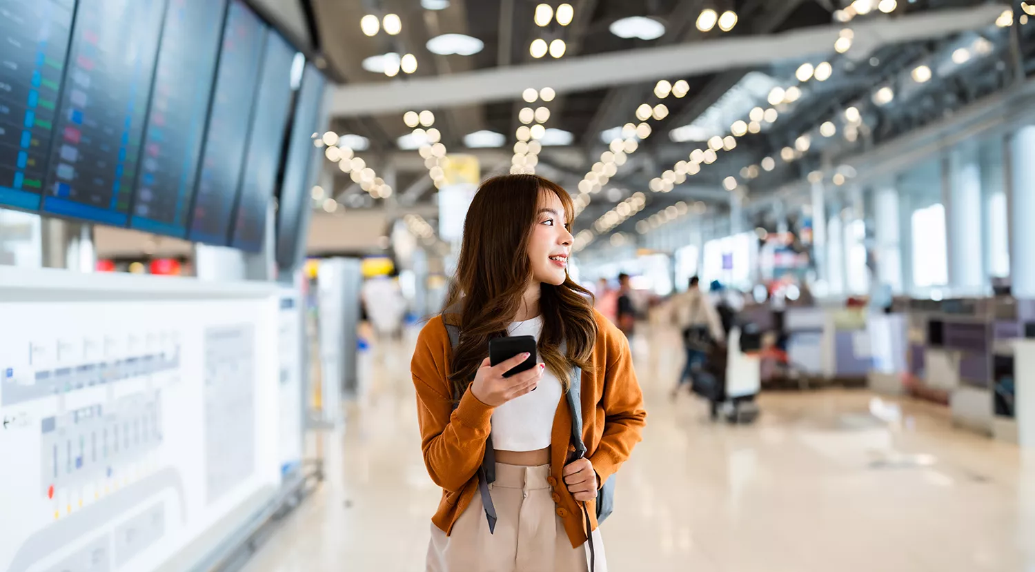 Young woman at an airport using a mobile phone for seamless global connectivity with a Travel eSIM